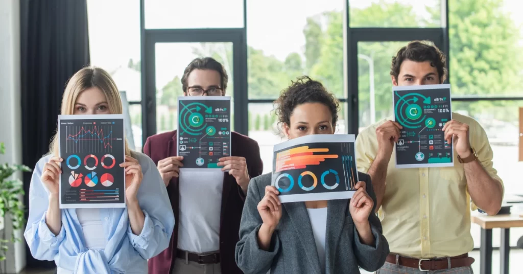 Yüzlerinin önünde merchandising performansını gösteren renkli analiz grafiklerini tutan dört profesyonel.